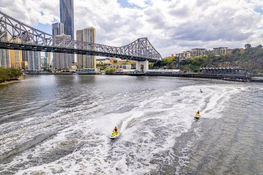 A river with two jet skis, a bridge, and city buildings in the background. 3