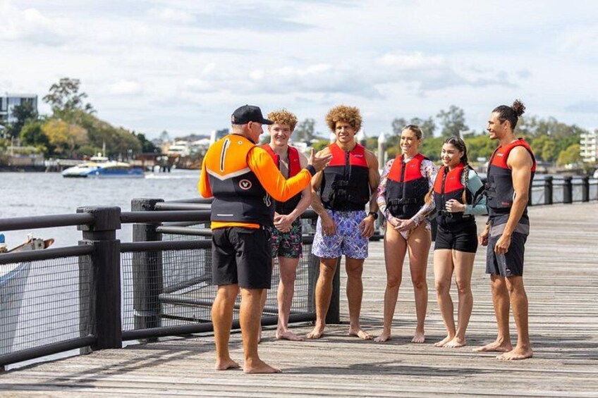 A group of people on a wooden boardwalk by a body of water, wearing life jackets. 4
