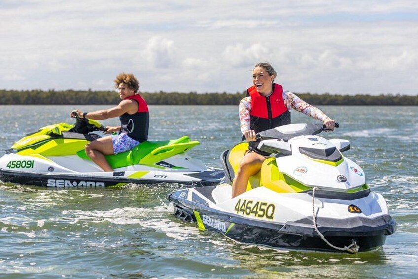 Two people on jet skis on a lake with trees in the background. 2