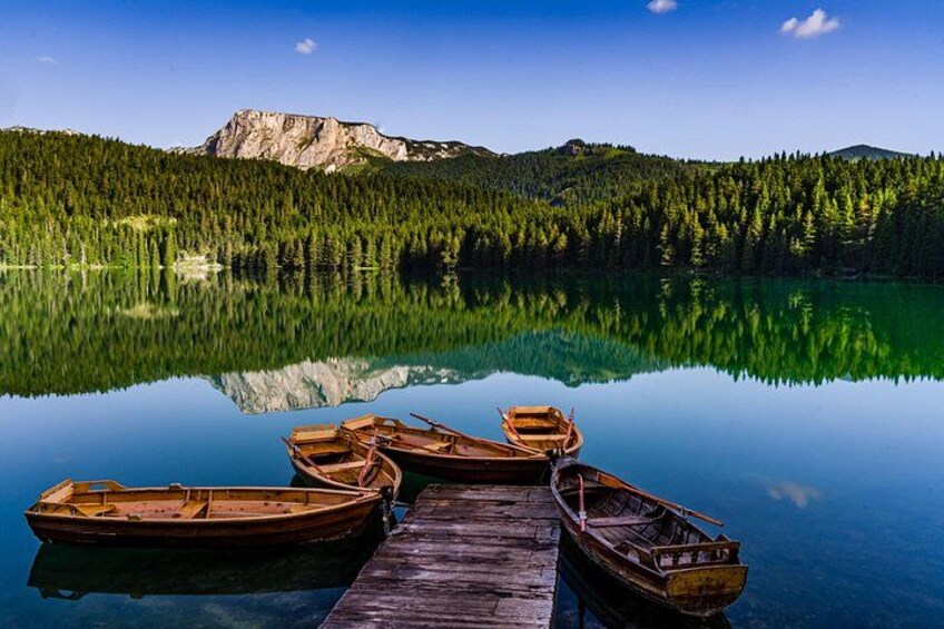 A calm lake with reflections of trees and mountains, wooden boats docked on a pier, and a clear sky. 5