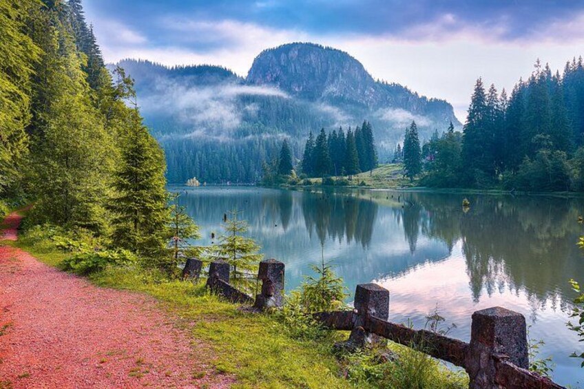 A serene lake surrounded by lush green trees and mountains, with a clear sky above. 2