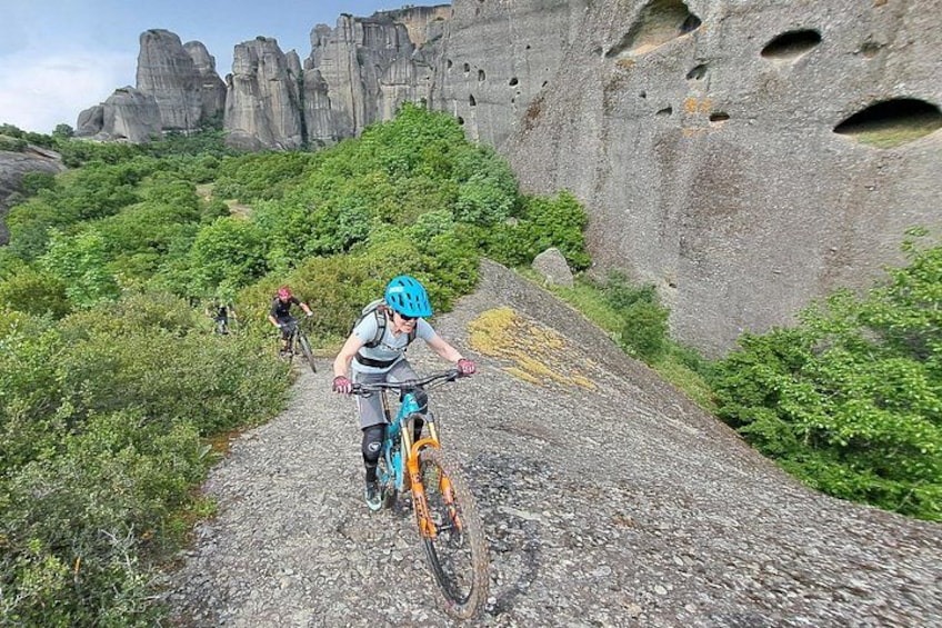 A mountain biker on a rocky trail with greenery and rock formations in the background. 1