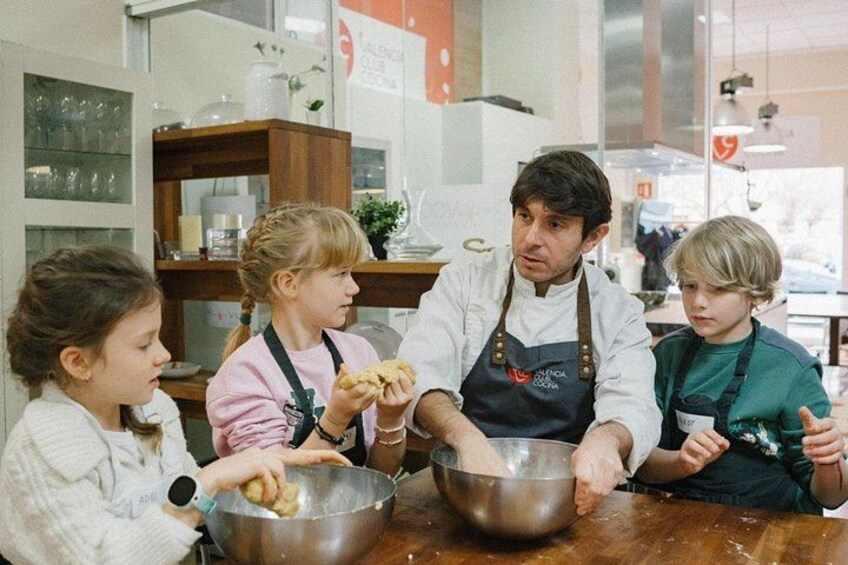 Eine Person in einer Kochschürze unterrichtet Kinder am Tisch beim Kochen. 3