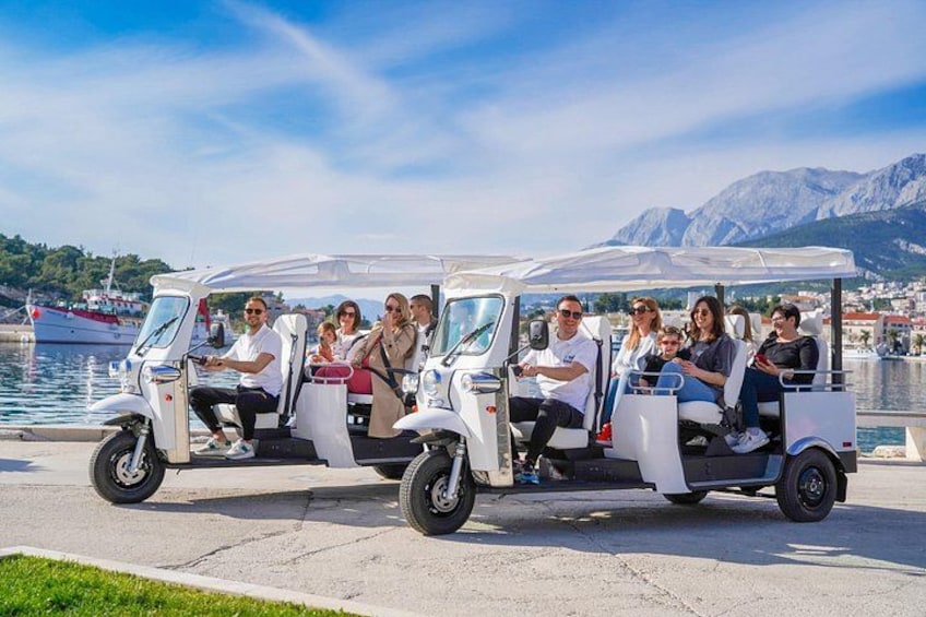 A group of people on a white golf cart by a waterfront with mountains in the background. 2