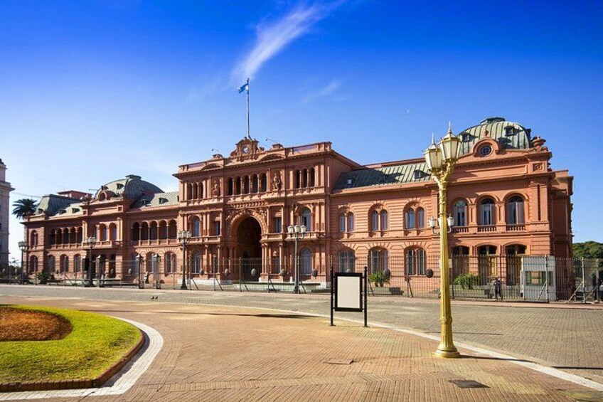 A large, ornate building with a central archway, a flagpole, and a well-maintained lawn. 1