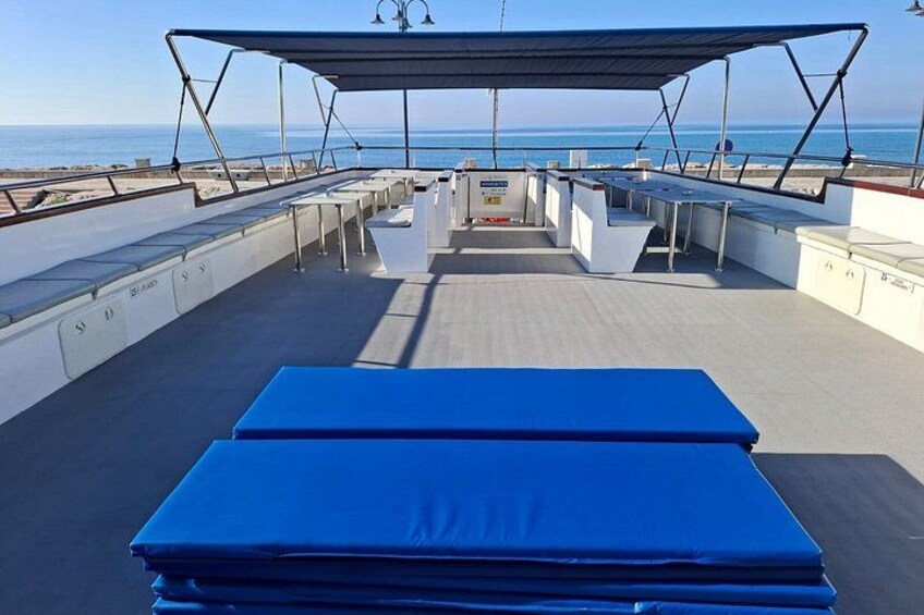 A boat deck with a blue cushioned area, white seating, and a covered section. 5
