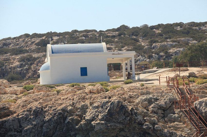 A white building with a blue door, surrounded by rocky terrain and hills. 3