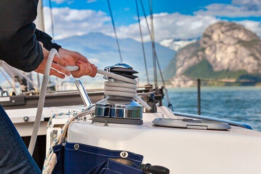 A person handling a rope on a sailboat with a mountainous landscape in the background. 4