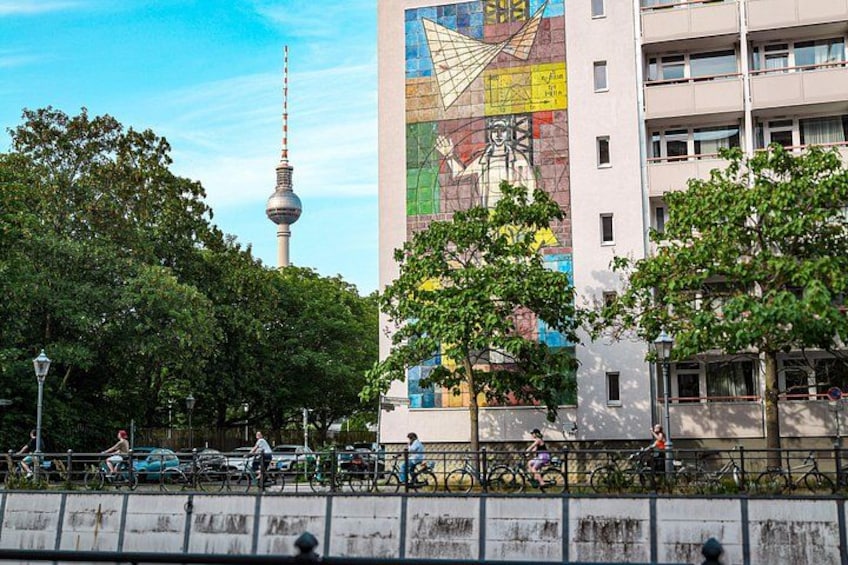 A cityscape with a prominent tower, a colorful mural on a building, and cyclists on a bridge. 4