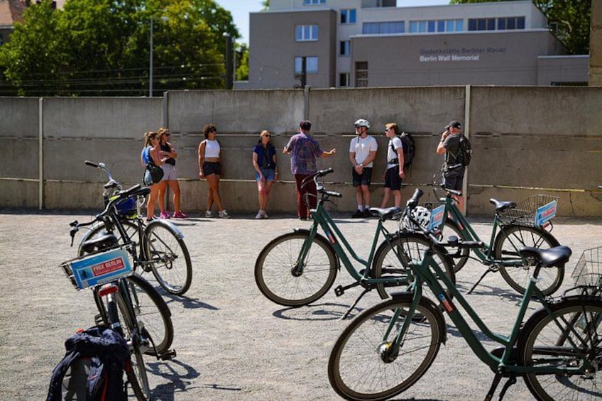 En grupp människor som står nära en vägg, med cyklar parkerade framför. 1
