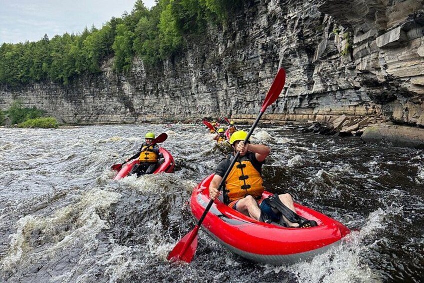 Two people kayaking on a river surrounded by rocky cliffs. 1
