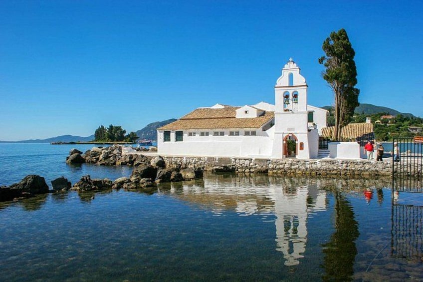 Une église blanche, dotée d’un clocher, se dresse au bord d’une mer calme, entourée de rochers et d’une eau cristalline. 2