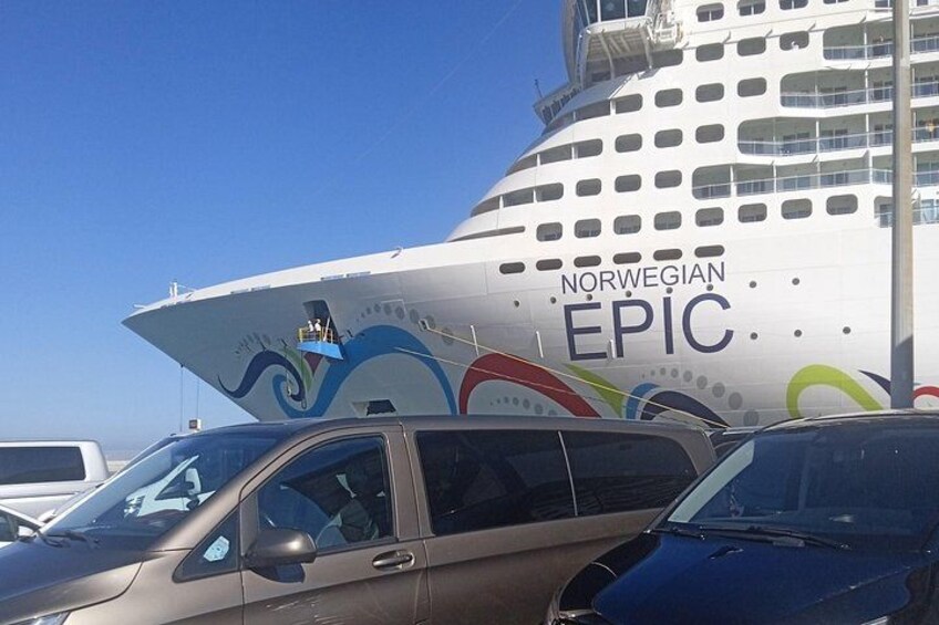 De cruiseschip Norwegian Epic ligt aangemeerd in een haven, met geparkeerde auto's ervoor. 1