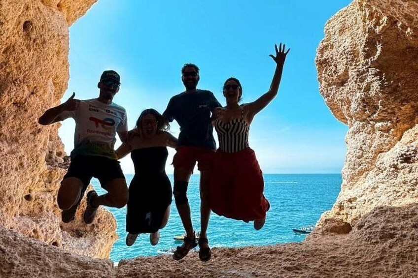 A group of people jumping in a rocky cave with a view of the sea. 1