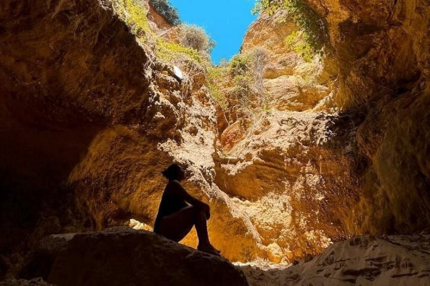 A person sitting on a rock in a canyon with steep rock walls and sparse vegetation. 5