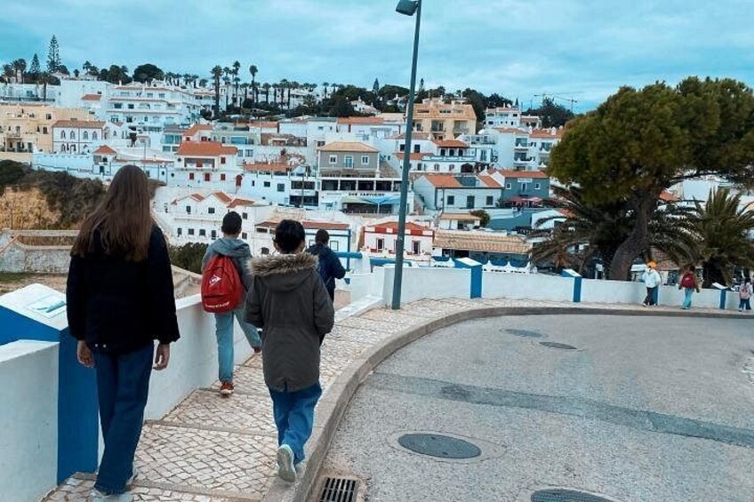 A coastal town with white buildings, a paved walkway, and a few pedestrians. 4