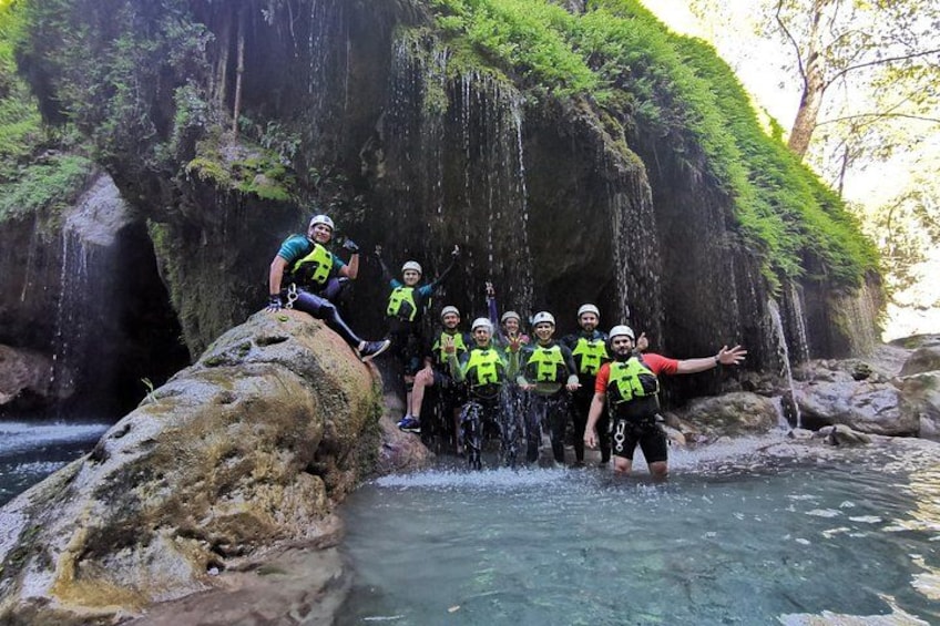 A group of people in safety gear near a waterfall in a forested area. 4