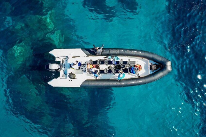 A white inflatable boat with people on board, floating on clear blue water. 3