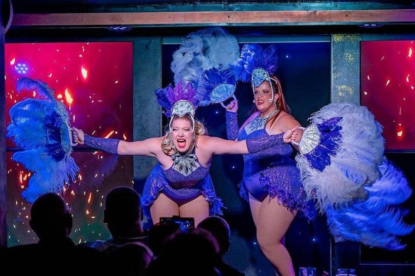 Two performers in blue and purple costumes with feathered headdresses on a stage. 4