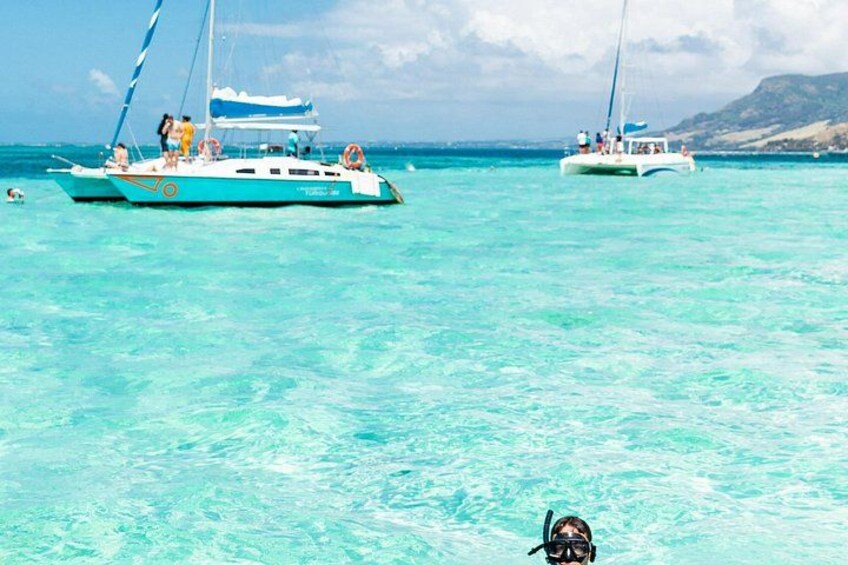 A turquoise boat with people on the water, a clear sky, and a distant mountain. 1