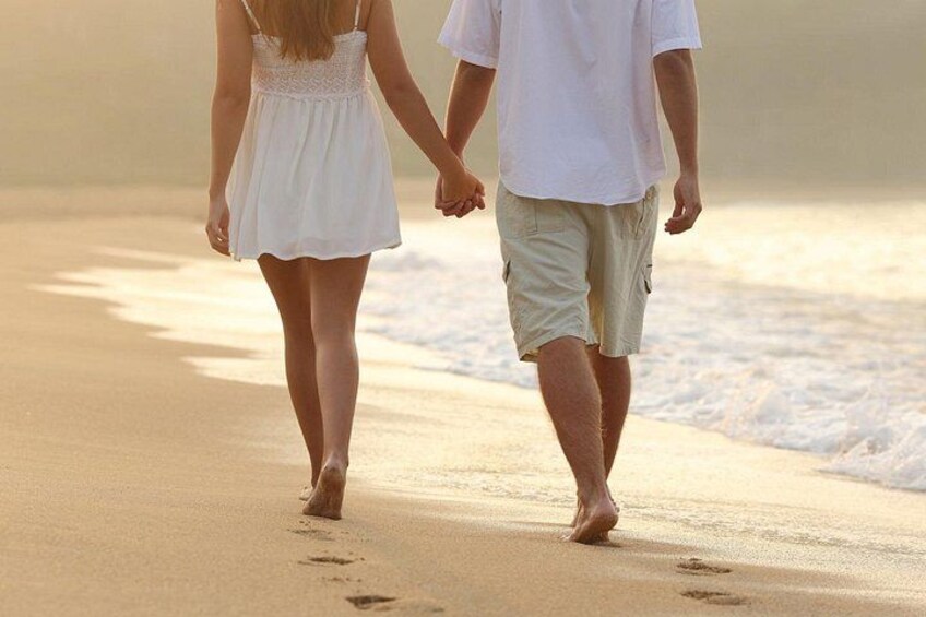 A couple walking hand in hand on a sandy beach with waves in the background. 2