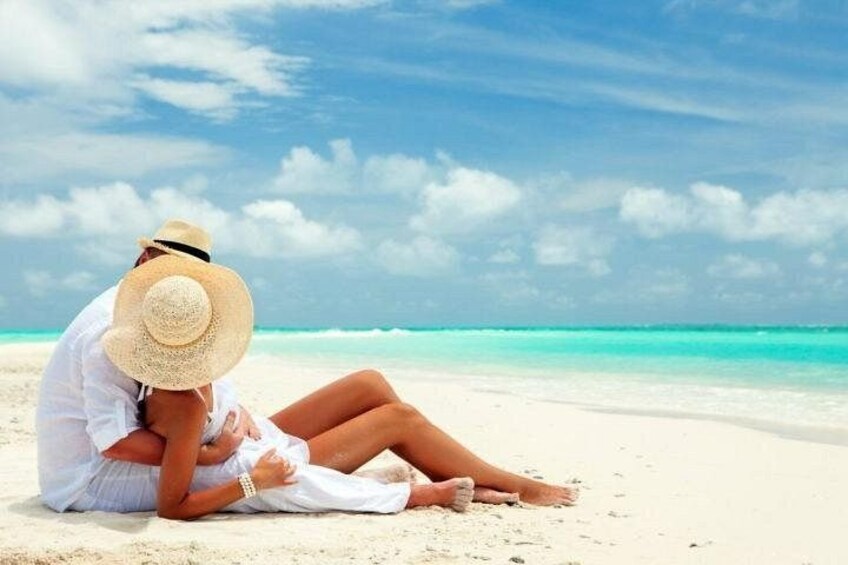 A person sitting on a sandy beach with a clear sky and turquoise water in the background. 3