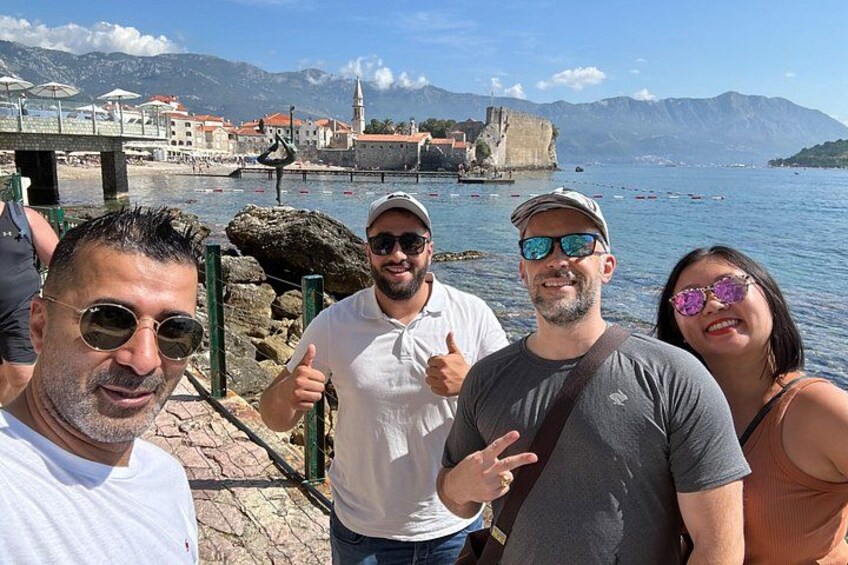 Un gruppo di persone vicino a una passeggiata sul lungomare, con un edificio storico e montagne sullo sfondo. 4