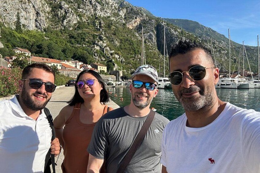 Un gruppo di persone vicino a un corso d'acqua con barche, un pendio roccioso e edifici sullo sfondo. 5