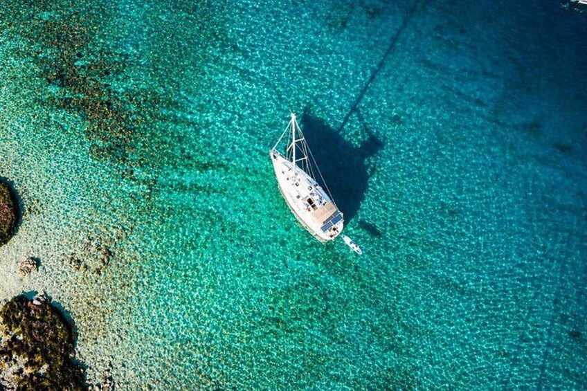A sailboat anchored in clear turquoise waters with a sandy beach and rocky outcrops in the foreground. 2