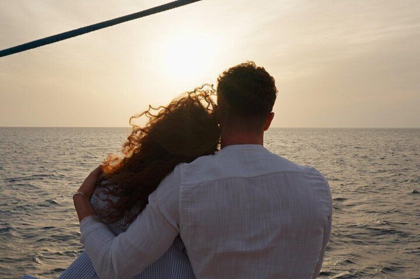 Una pareja se abraza en un barco mientras el sol se pone al fondo. 2