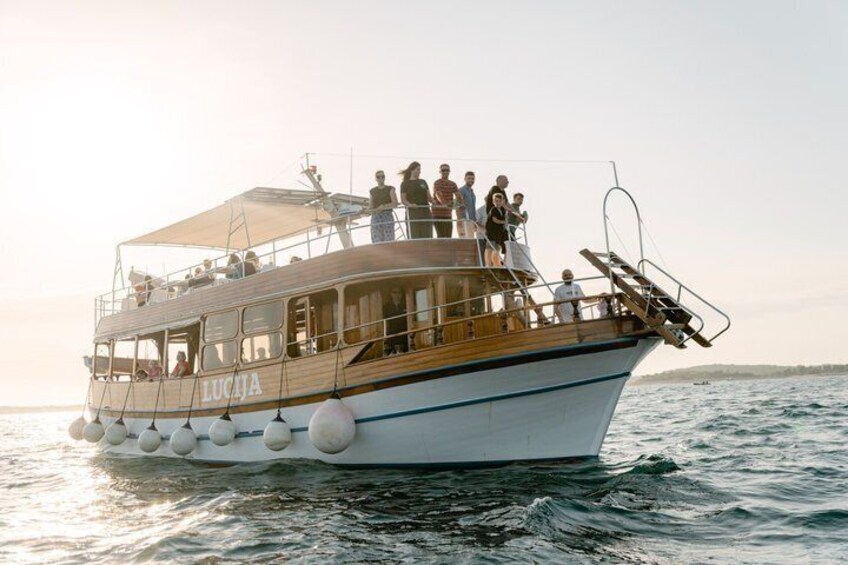 A boat named 'LUČJA' with passengers on deck, sailing on water. 1