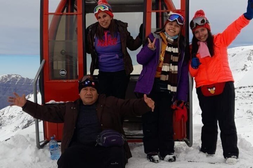 A group of people in winter gear on a ski lift with snow-covered mountains in the background. 2