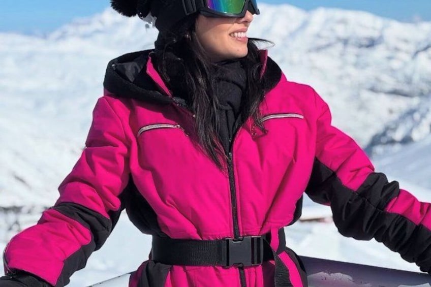 A person in a bright pink jacket with black accents, standing on a snowy mountain with a clear sky. 3