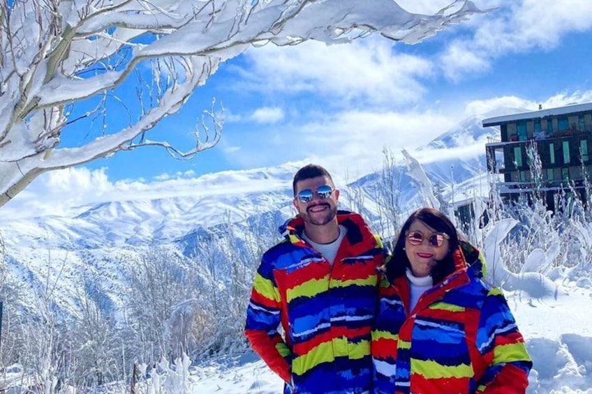 A couple in colorful winter jackets standing in a snowy landscape with mountains in the background. 2