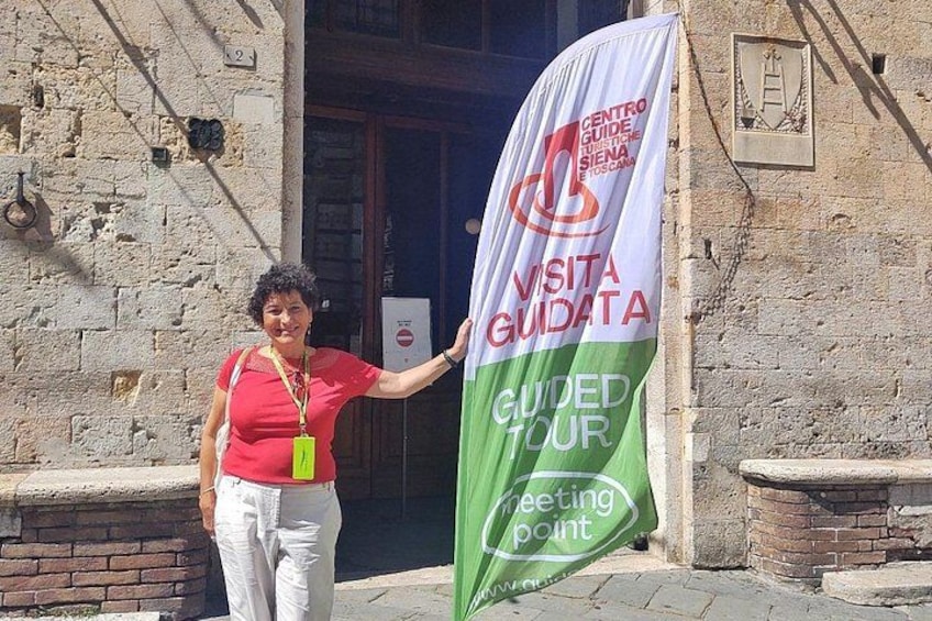 En person står ved et banner med teksten 'VISITA GUIDATA' og 'GUIDED TOUR' på en bygningsfacade. 1