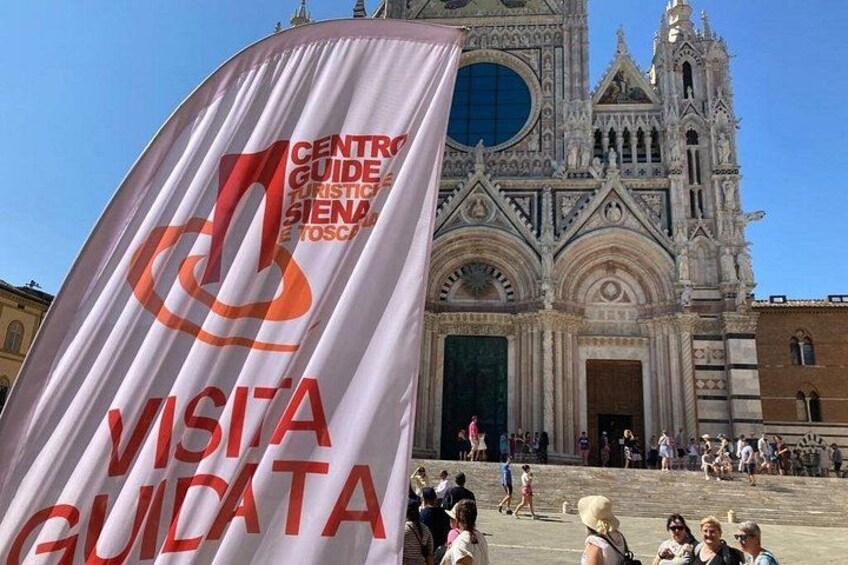 En banner med teksten 'VISITA GUIDATA' foran en katedral. 2