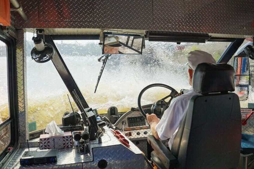 A person driving a vehicle with a steering wheel, dashboard, and windshield wipers. 5