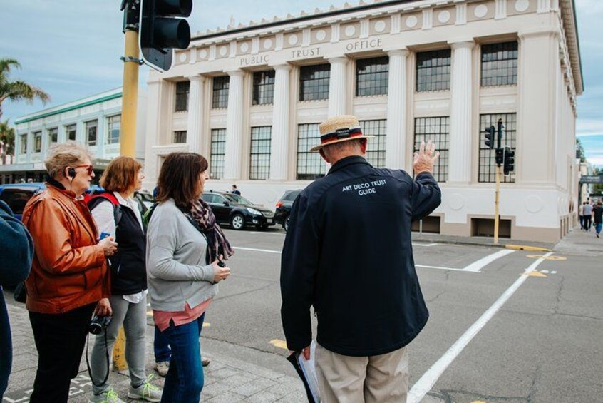Un grupo de personas de pie en una acera frente a un edificio con la leyenda 'Public Trust Office'. 1