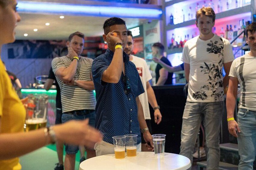 A bar setting with people standing around a table with drinks. 2