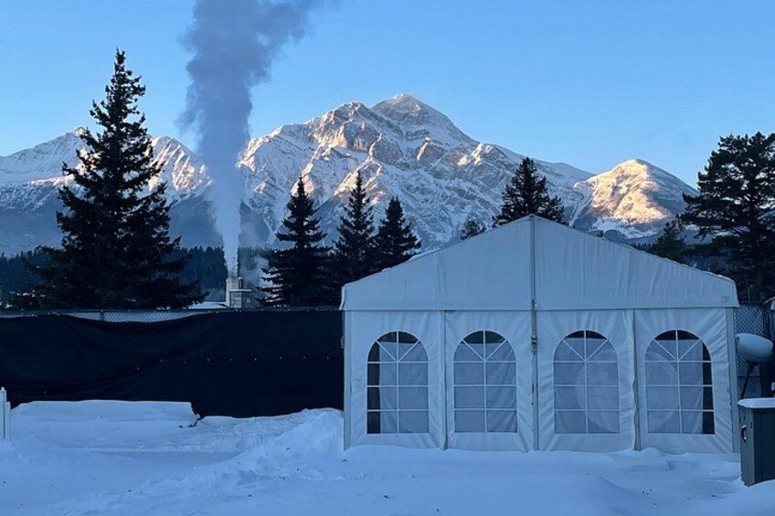 A snow-covered landscape with a white tent, a mountain, and a smoke plume. 2