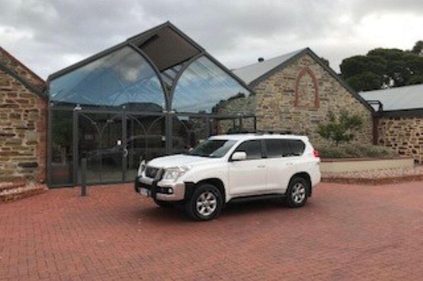 A white SUV parked in front of a building with a glass entrance and stone walls. 5