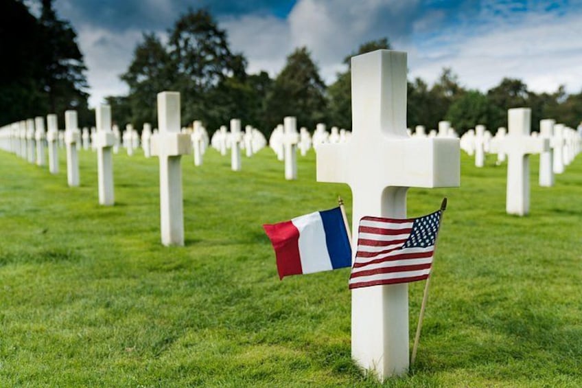 Ein Friedhof mit weißen Kreuzen und französischen sowie US-amerikanischen Flaggen. 1