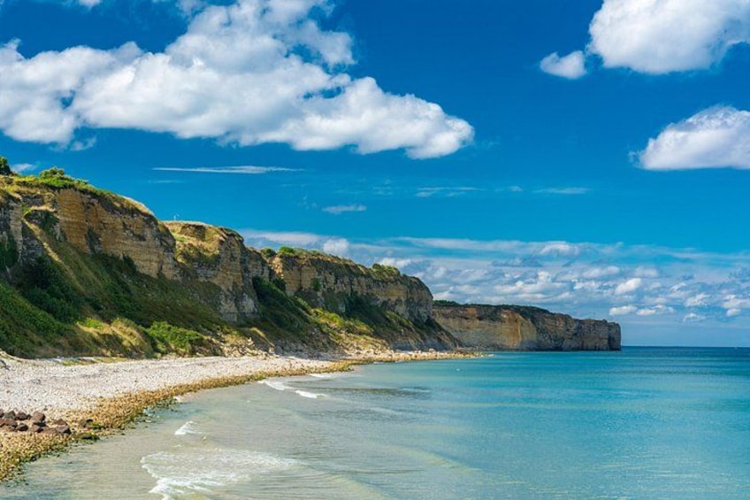 Eine Küstenlandschaft mit Klippen, einem Sandstrand und klarem, blauem Wasser. 2