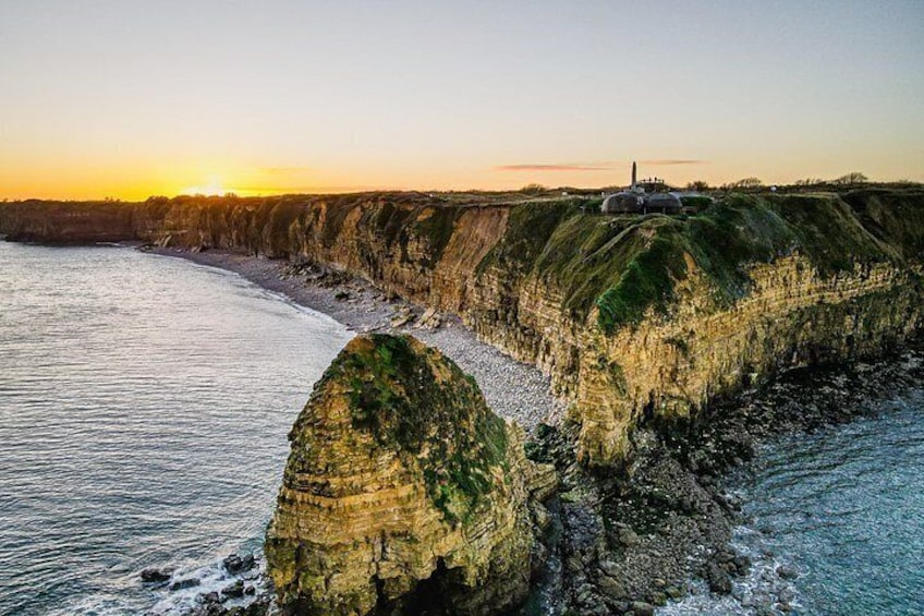 A coastal cliff with a lighthouse, ocean waves, and a sunset. 2