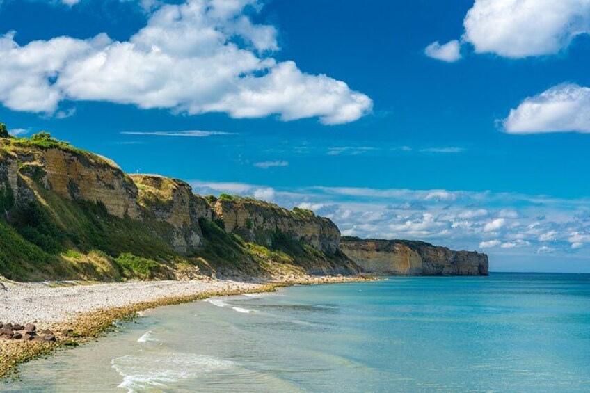A coastal landscape with cliffs, a sandy beach, and clear blue waters. 3