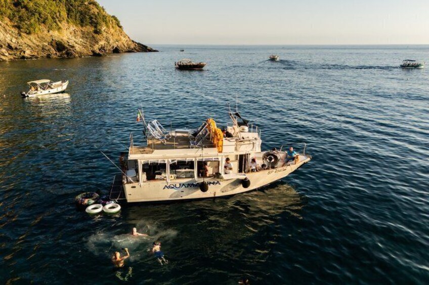A boat named AQUAMMA on calm waters with a rocky coastline and other boats in the distance. 2