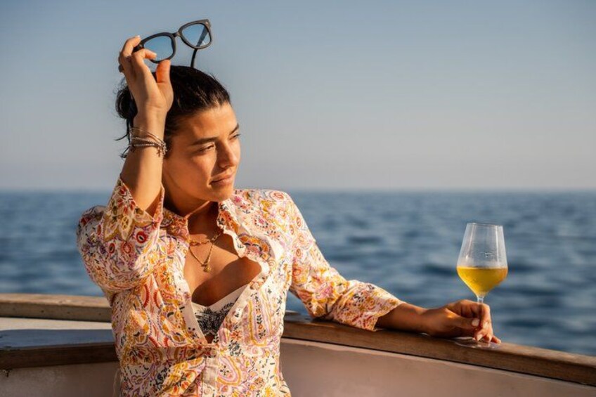 Een persoon houdt een wijnglas vast op een boot, met de oceaan op de achtergrond. 4