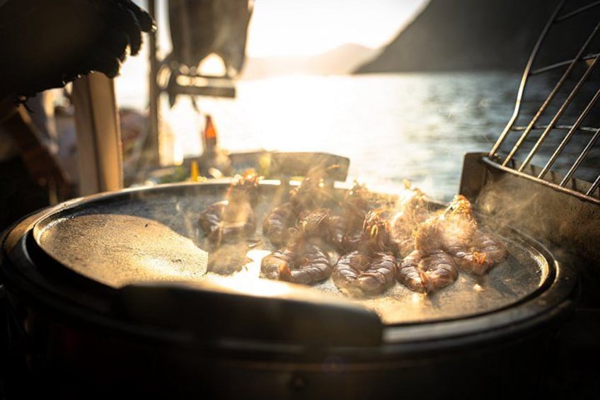 En grill där mat tillagas över öppen eld, med en vattenyta och berg i bakgrunden. 3