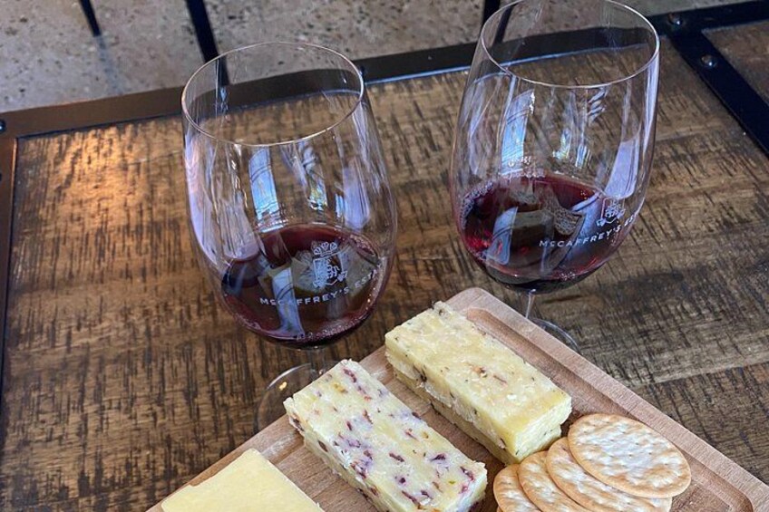 Two glasses of red wine, a wooden cutting board with cheese and crackers, and a metal table. 3