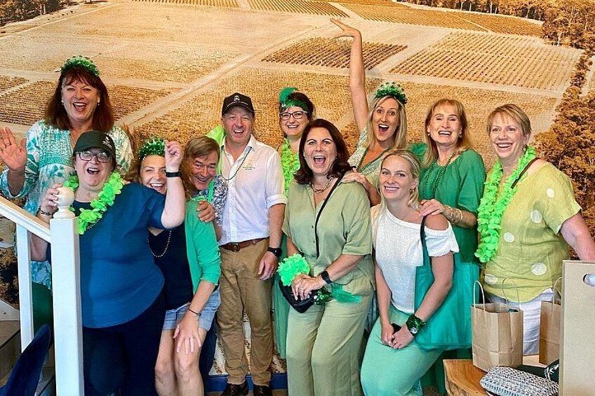 A group of people in green attire with leis, standing on a staircase. 4
